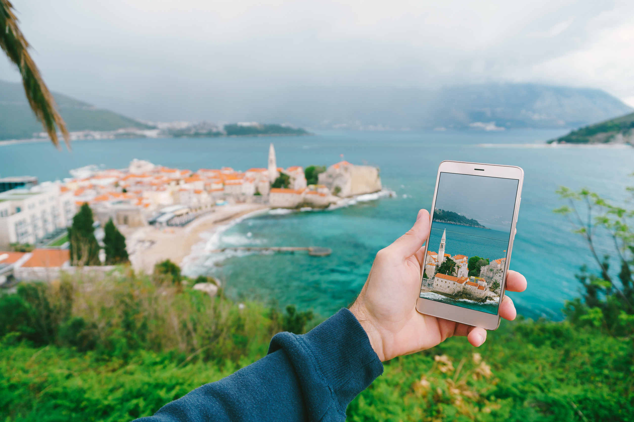 mans hand holds a smartphone with a photo of architecture left the old town