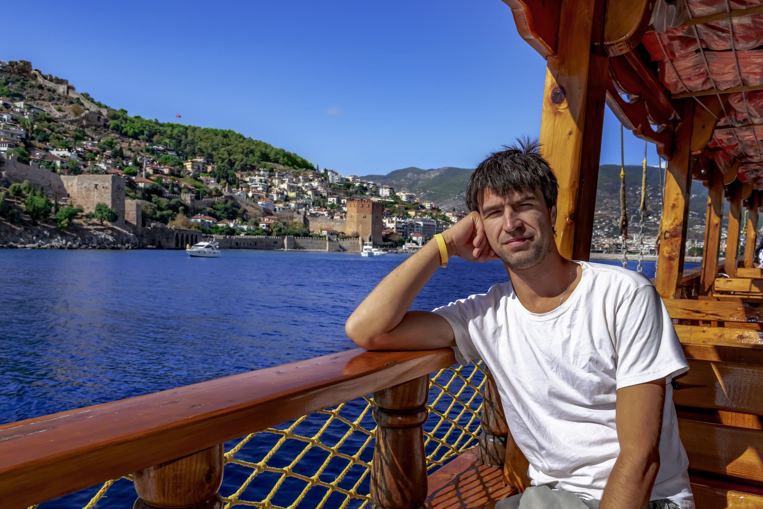 happy smiling man sits on the deck of a wooden boat against the backdrop of the landscape of alanya